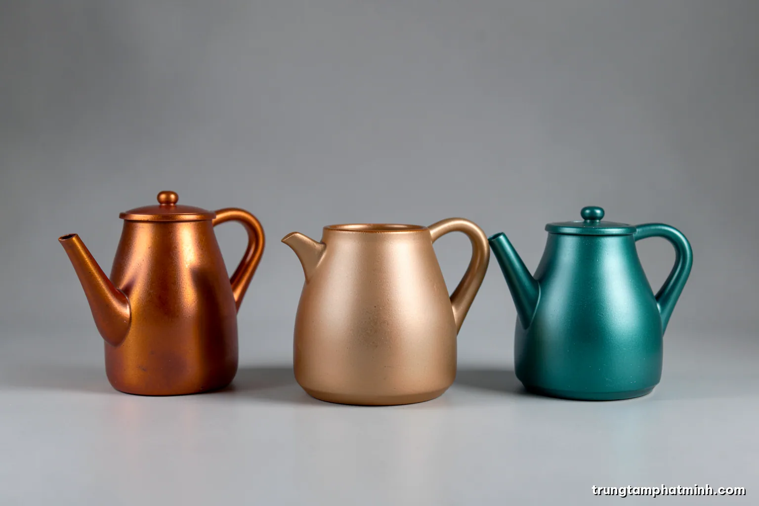 Studio still life of three matte ceramic kettle prototypes in slightly different silhouettes on a seamless grey backdrop, raking side light, wide shot, slate and ivory palette